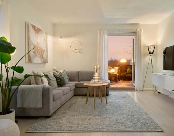 A living room with a grey couch, a wooden table, a television, and a large window with a view of the outside.