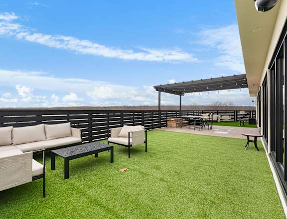 A patio with a white couch, black table, and a green lawn.