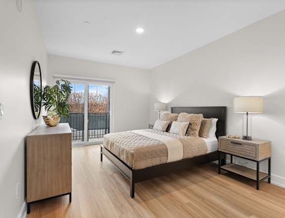 A bedroom with a large bed, a wooden nightstand, and a plant on a cabinet.