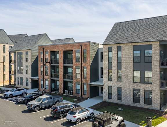 A parking lot with cars and a building with a mix of brick and siding exterior.