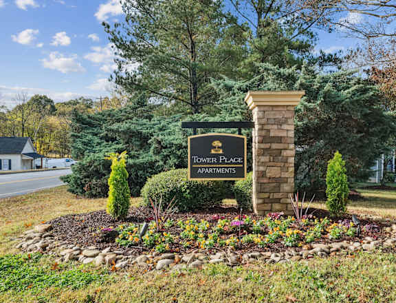 A sign for Tower Place Apartments is surrounded by flowers and greenery.