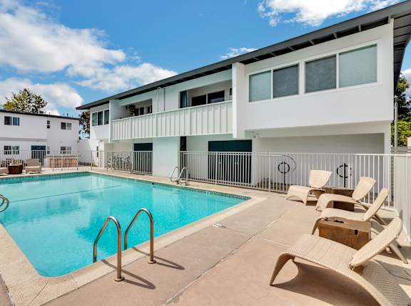 A swimming pool surrounded by chairs and a white building in the background.