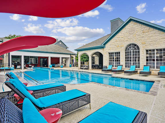 A large swimming pool with lounge chairs and a building in the background.