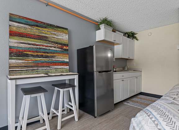 A kitchen area with a refrigerator, bar stools, and a painting on the wall.