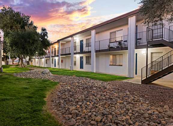 A sunset view of apartment buildings with balconies and a gravel path.