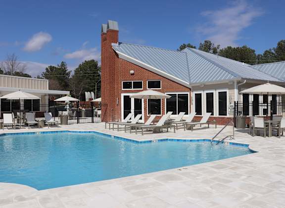 A pool area with a building and lounge chairs at Carlton Park Apartment Homes, Mississippi
