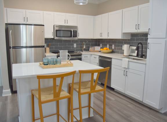 a kitchen with white cabinets and a counter with two chairs