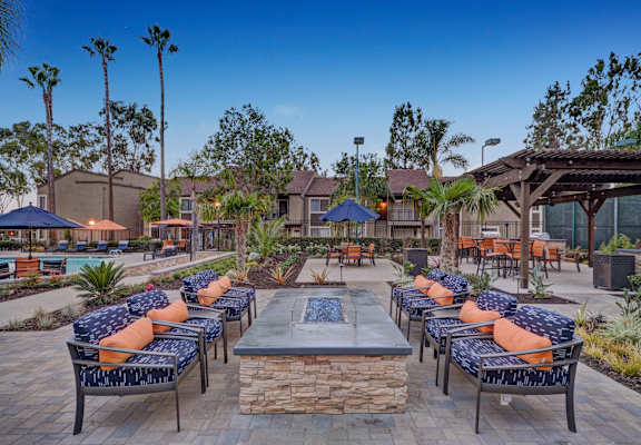 A patio with a fire pit surrounded by chairs and tables.