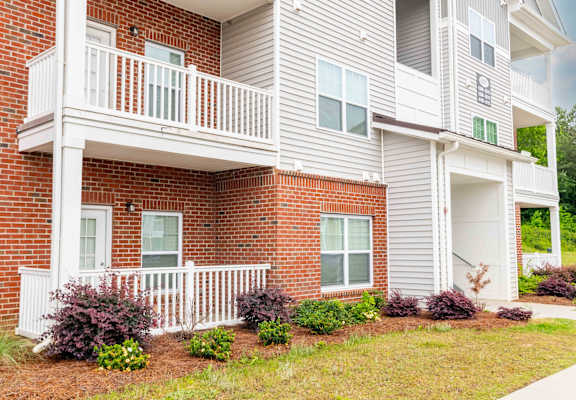 A two-story apartment building with a balcony and a small garden in front.
