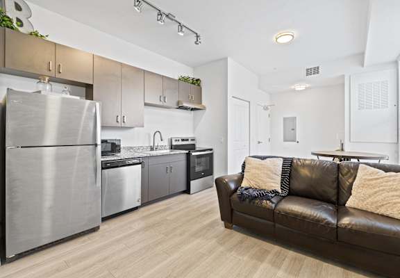 a living room with a leather couch and a kitchen with stainless steel appliances