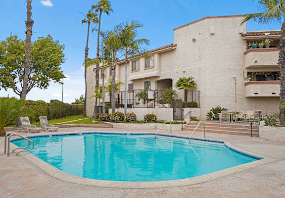 A swimming pool in front of a building with palm trees.