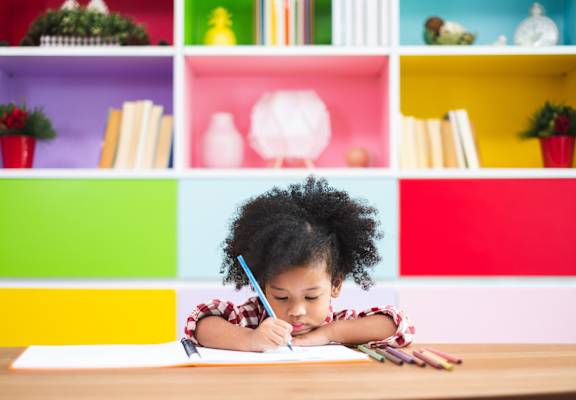 A child is writing on a piece of paper with a blue pencil.