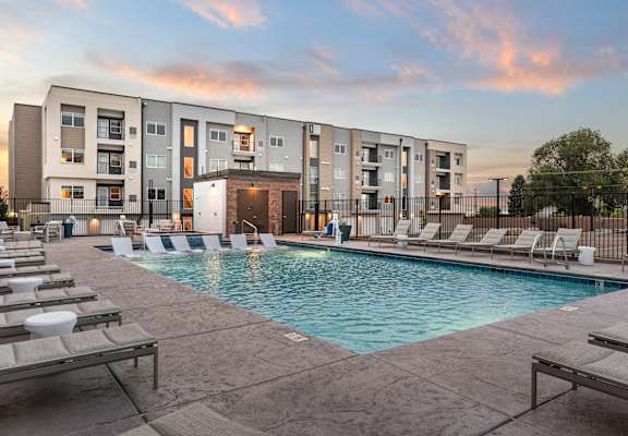 A swimming pool surrounded by lounge chairs in front of apartment buildings.