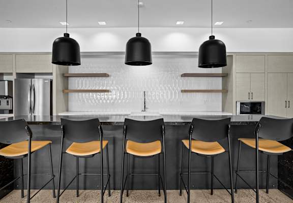 A modern kitchen with black chairs and a white backsplash.