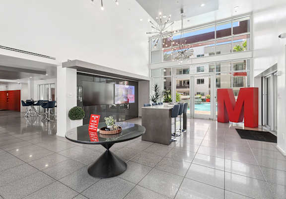 A large foyer with a black table in the middle and a red letter M on the wall.