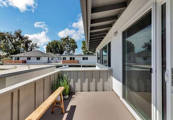 A wooden bench is on a patio with a glass door.