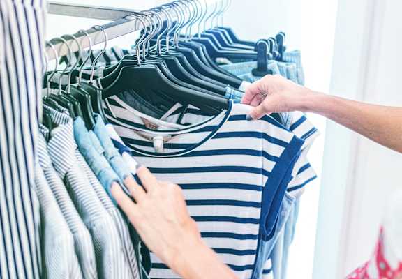 A person is holding a striped shirt in front of a rack of clothes.