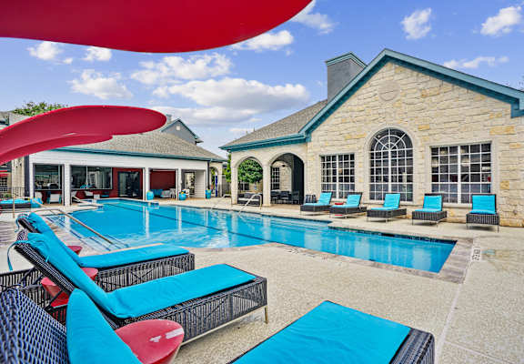 A large swimming pool with lounge chairs and a building in the background.