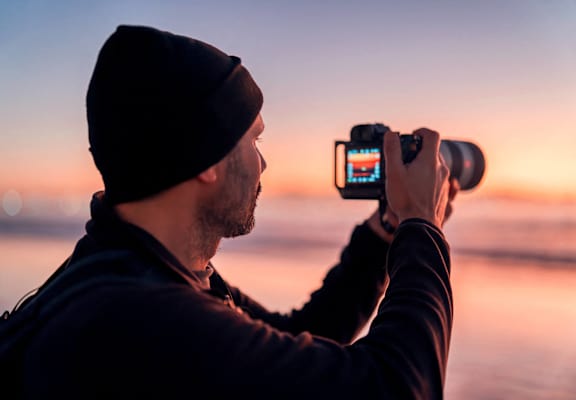 a man taking a picture of a sunset with a camera on his phone