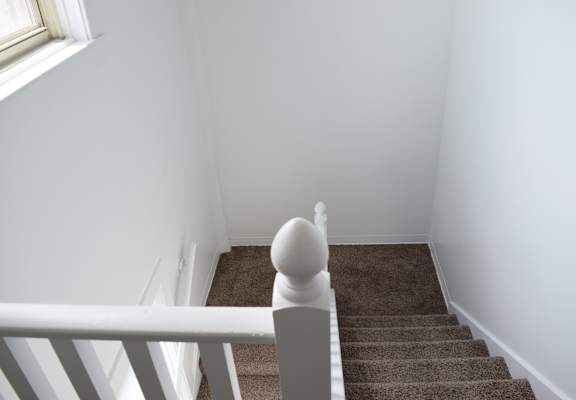 A staircase with a white railing and brown carpet.