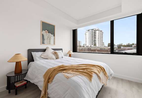 A bedroom with a large bed and a view of a building outside the window.