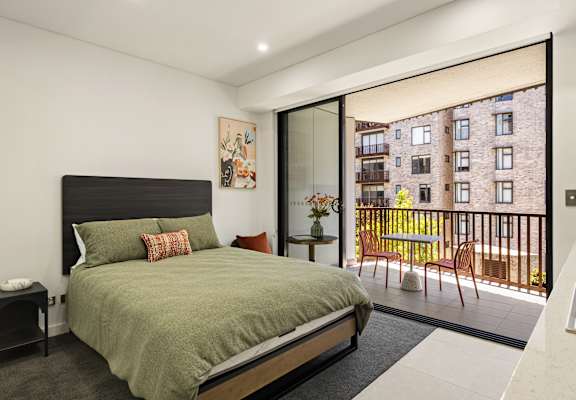 A bedroom with a large bed and a view of a building outside through a glass door.