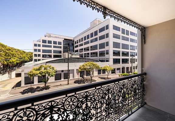 A balcony with a black railing overlooks a large white building with many windows.