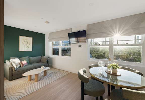 A modern living room with a grey couch, a glass table, and a television mounted on the wall.