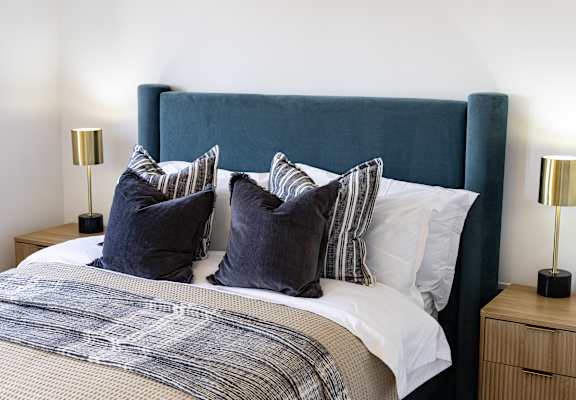A bed with a blue headboard and striped pillows.