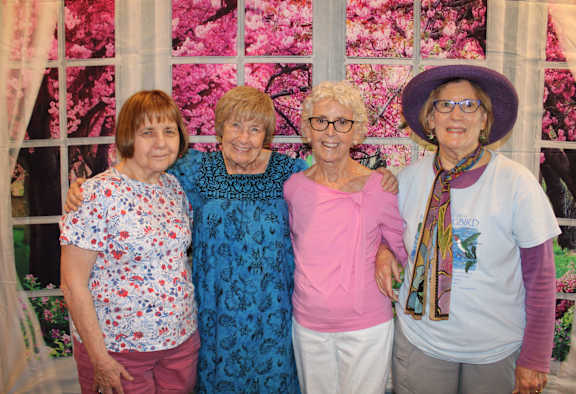 Four women standing together in front of a floral backdrop.