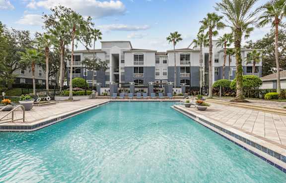A swimming pool in front of a building surrounded by palm trees.