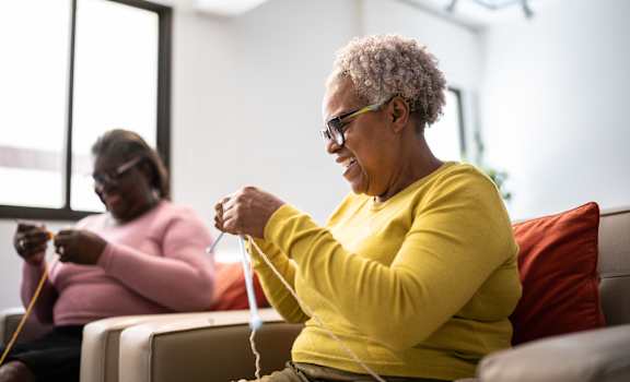Two women knitting in a bright room.