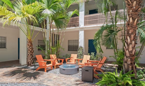 a patio with a fire pit and chairs in front of a building