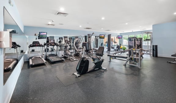a spacious fitness room with cardio equipment and flat screen tvs
