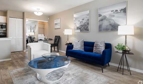 A living room with a blue couch and a glass coffee table.