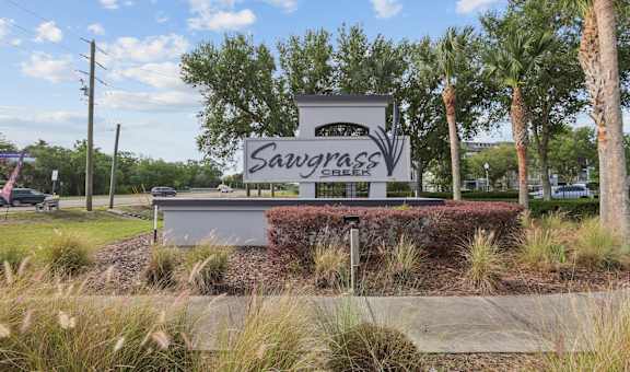A sign that says Sawgrass in front of some trees.