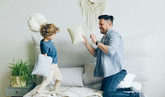 A man and a child are playing with pillows on a bed.