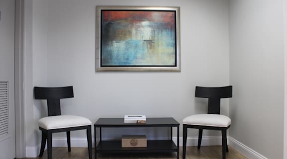 A painting hangs on a wall above a black coffee table with two chairs on either side.