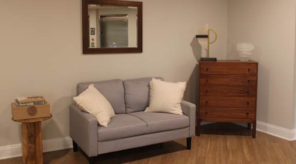 A grey couch with a white pillow sits in front of a mirror.