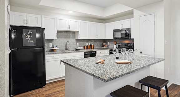 a kitchen with a granite counter top and a black refrigerator at La Ventura Apartments, Plano, TX