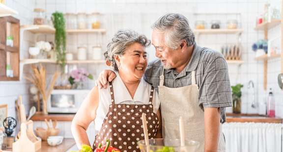 an older couple laughing while preparing food in the kitchen