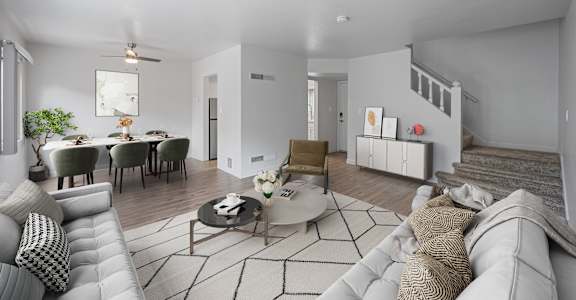 A modern living room with a grey sofa, a coffee table, and a dining table set up at Hillsdale Garden Apartments, San Mateo