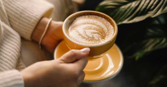 A person is holding a cup of coffee with a latte art design on top.