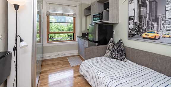 A bedroom with a bed, a television, and a window with a view of the city.