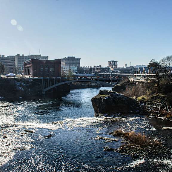 A river flows through a rocky landscape with buildings in the background.
