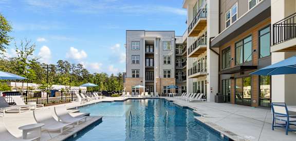 A swimming pool with white lounge chairs and apartment buildings in the background.