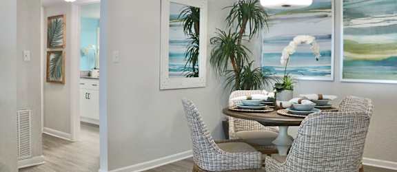 A dining room with a table set for two and a potted plant.