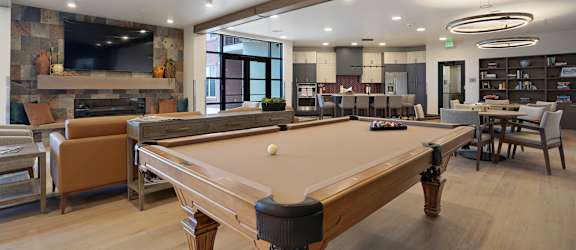 A pool table is in the middle of a room with a bar and a TV.