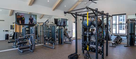 A gym with a variety of equipment including a weight bench, a leg press machine, a cable machine, a squat rack, a rowing machine, a treadmill, a stationary bike, a kettlebell