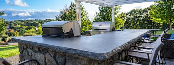 a stone bar with two bbq pits under a white roof on a patio